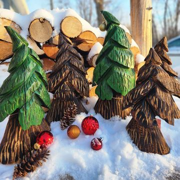 Wooden Christmas trees and ornaments arranged in the snow with stacked logs.