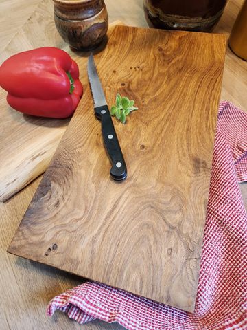 Wooden cutting board with a small knife, a red bell pepper, and herbs on a kitchen towel.