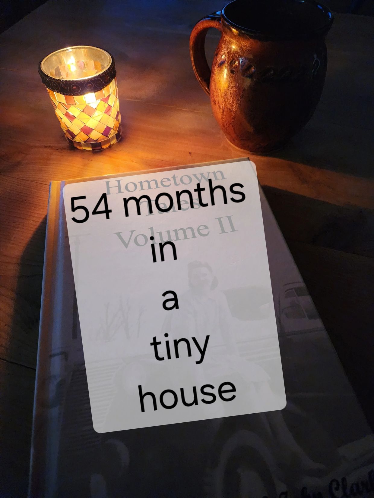Candlelit cozy scene with a book and a rustic mug on a wooden table.