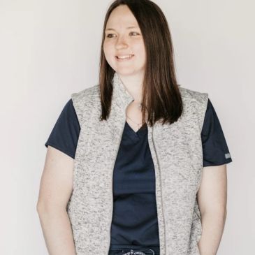 Smiling woman wearing a gray vest over a navy blue shirt.
