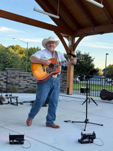 Man in cowboy hat playing acoustic guitar outdoors.