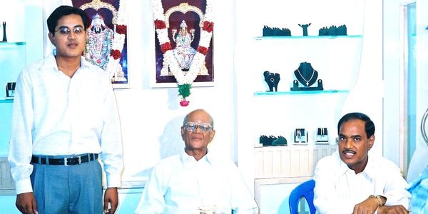 Three men in a bright room with religious pictures and jewelry displays.