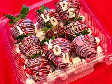 Chocolate-covered strawberries with love-themed decorations in a clear container.