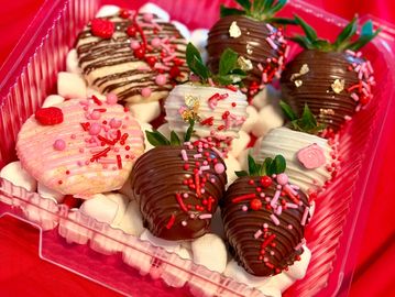 Decorated chocolate-covered strawberries and cookies in a clear plastic box with marshmallows.