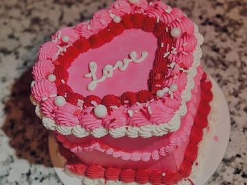 Heart-shaped cake decorated with pink, red, and white frosting and the word "Love".