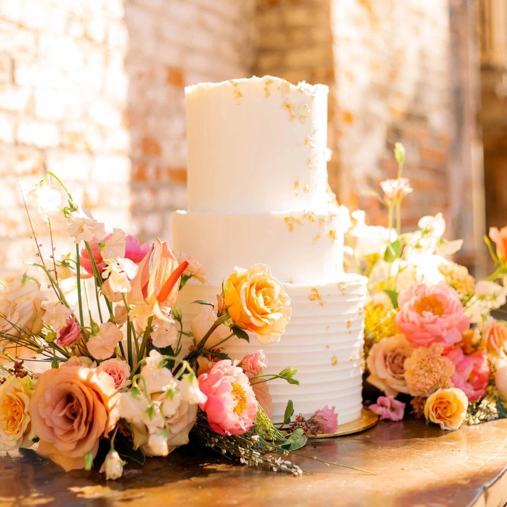 Elegant two-tier white cake adorned with pastel flowers and gold accents.