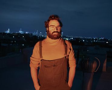 @vrunt on roof-orange light covers him with blue night sky & Manhattan skyline lit up in background