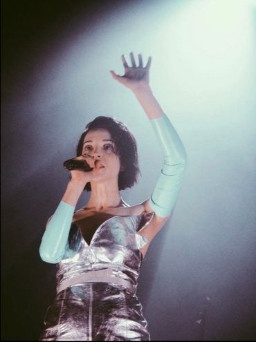 Musician St Vincent in silver metallic dress&light blue latex gloves,left arm in air,singin into mic