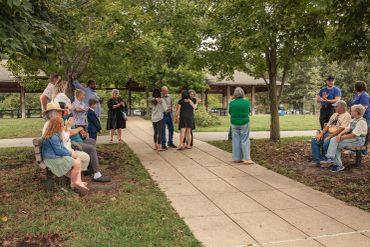 People gathered in a park, socializing and sitting on benches.