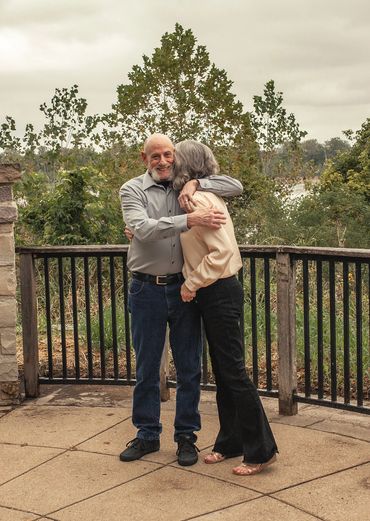 An elderly couple sharing a warm embrace outdoors.