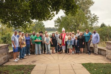 A large group of diverse people posing outdoors under leafy trees.