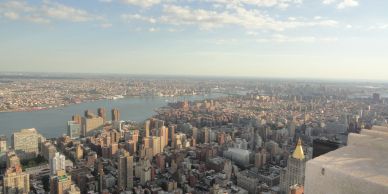 Aerial view of a city skyline with a river and many buildings under a partly cloudy sky.