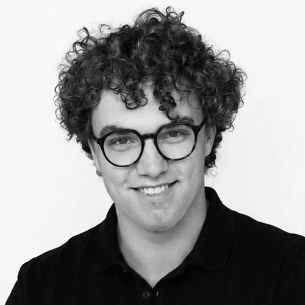 Junger Mann mit lockigem Haar und Brille lächelt.