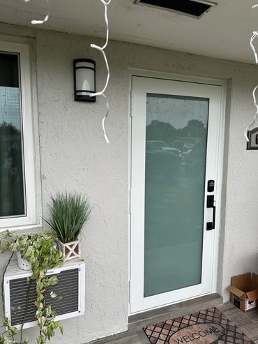Modern white front door with frosted glass and plants outside.
