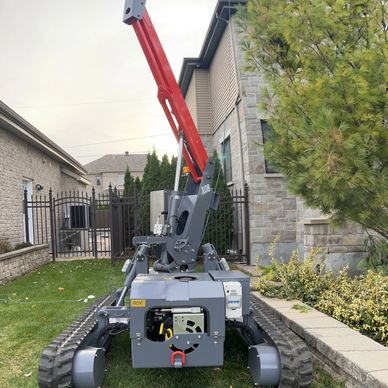Compact tracked robotic arm with red boom outdoors near buildings.