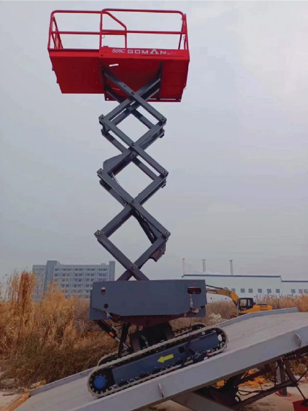 Red scissor lift elevated on a construction site ramp.