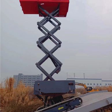 A red scissor lift extended outdoors near buildings and dry grass.