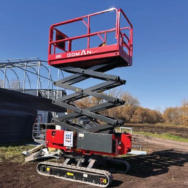 Red scissor lift with tracked base on a dirt ground under clear blue sky.