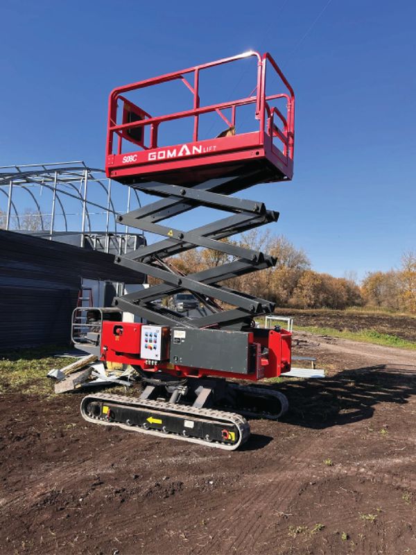 Red Goman scissor lift raised outdoors on dirt ground near construction.