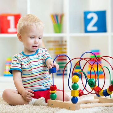 A toddler playing with a colorful bead maze toy indoors.
