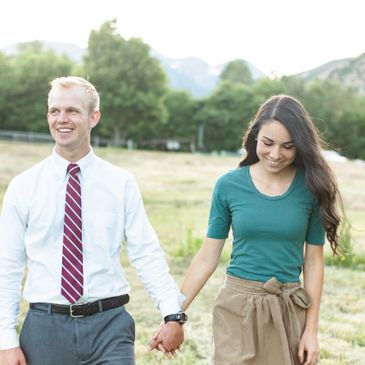 A smiling couple holding hands and walking outdoors in a sunny field.