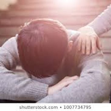 Person with head down being comforted by another's hand on their shoulder.