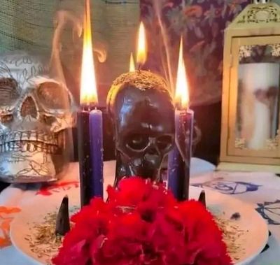 A ritualistic arrangement with skulls, burning candles, and red flowers.