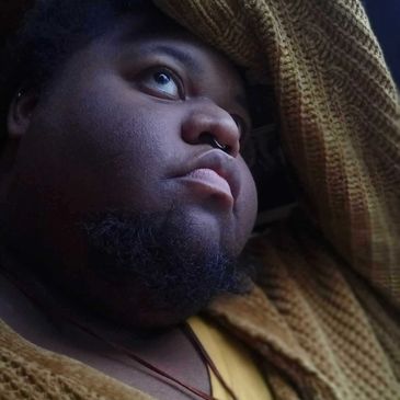 Portrait of a thoughtful person looking upward, wearing a textured brown garment.