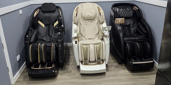 Three different massage chairs lined up in a room with gray walls.