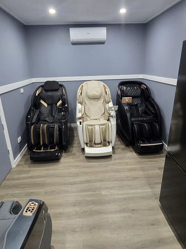 Three massage chairs in a minimalistic room with gray walls and wooden floor.