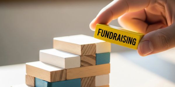 Hand placing a block labeled 'FUNDRAISING' on a wooden staircase.