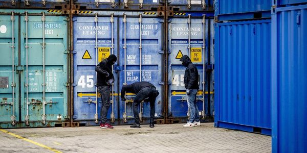 Three people inspecting blue shipping containers.