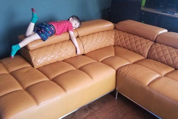 A child lies face down on a tan leather sectional sofa.
