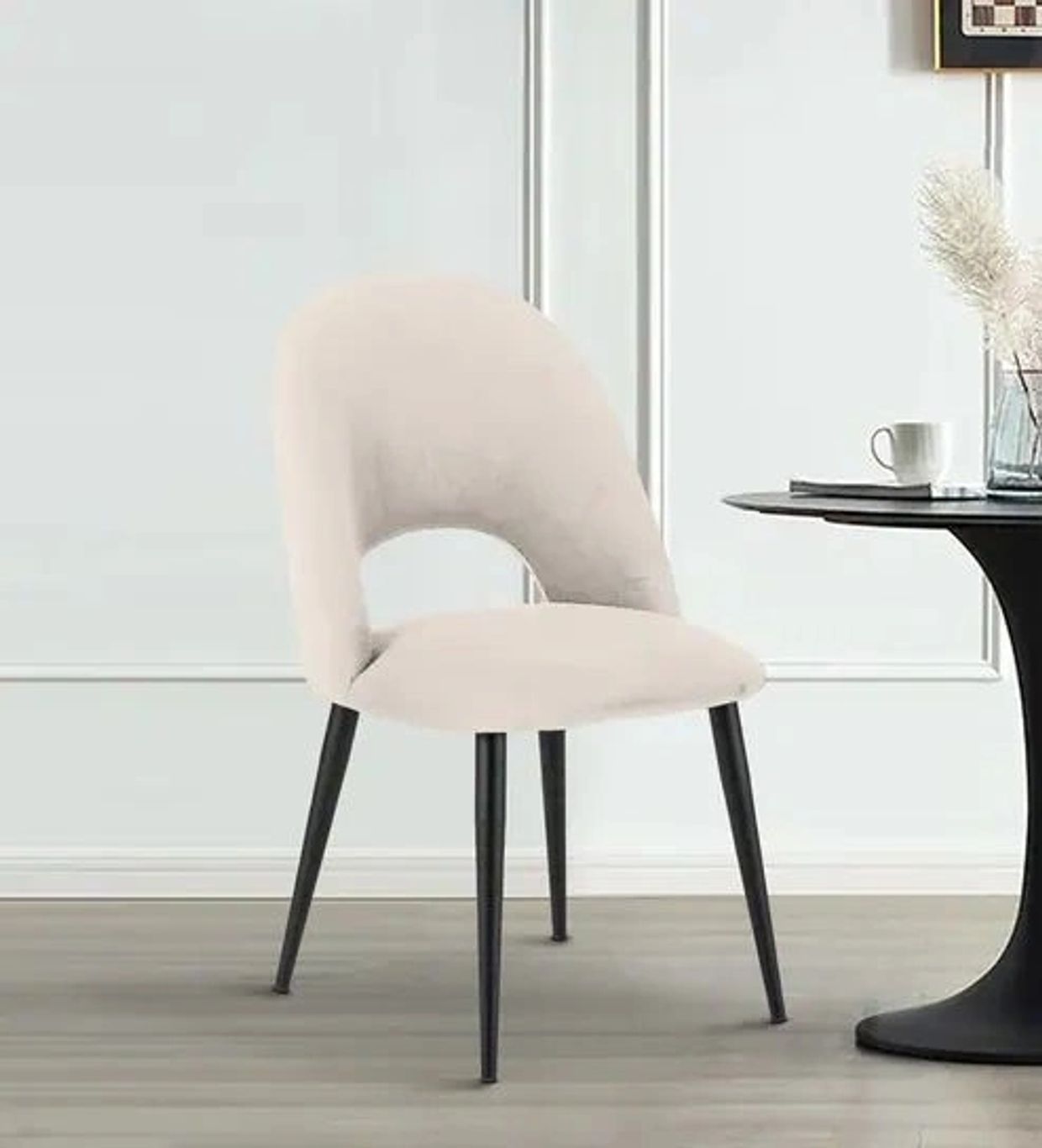 Modern beige upholstered chair with black legs beside a round table.