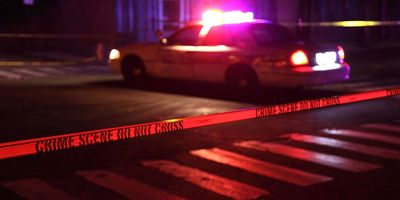 Police car with flashing lights behind crime scene tape at night.