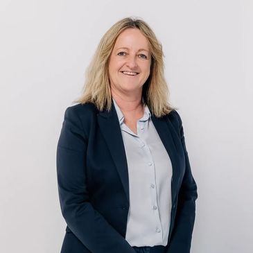 Professional woman in navy blazer and trousers smiling against a white background.