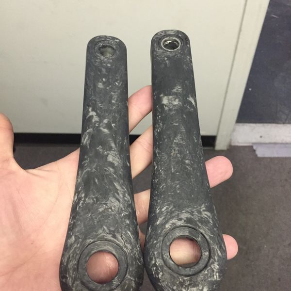 Two dark marbled bicycle crank arms held in hand.