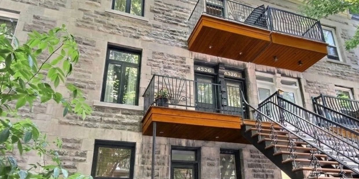 Façade en pierre d'un triplex montréalais avec balcons en bois, escalier extérieur & fer forgé forgé