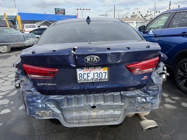 Rear of a blue Kia Optima with significant damage to the bumper and trunk.