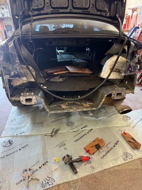 A car with its rear bumper removed, tools and gloves laid out on a mat.