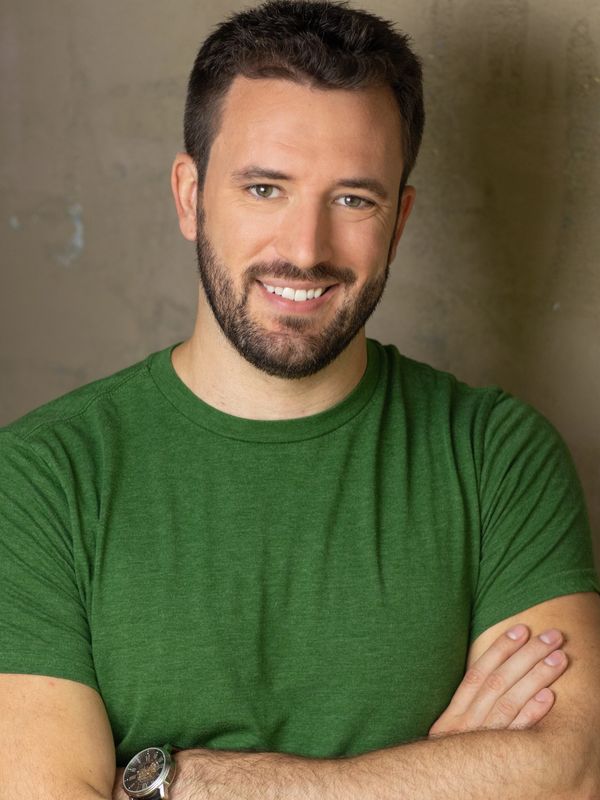 Smiling man in a green shirt with arms crossed.
