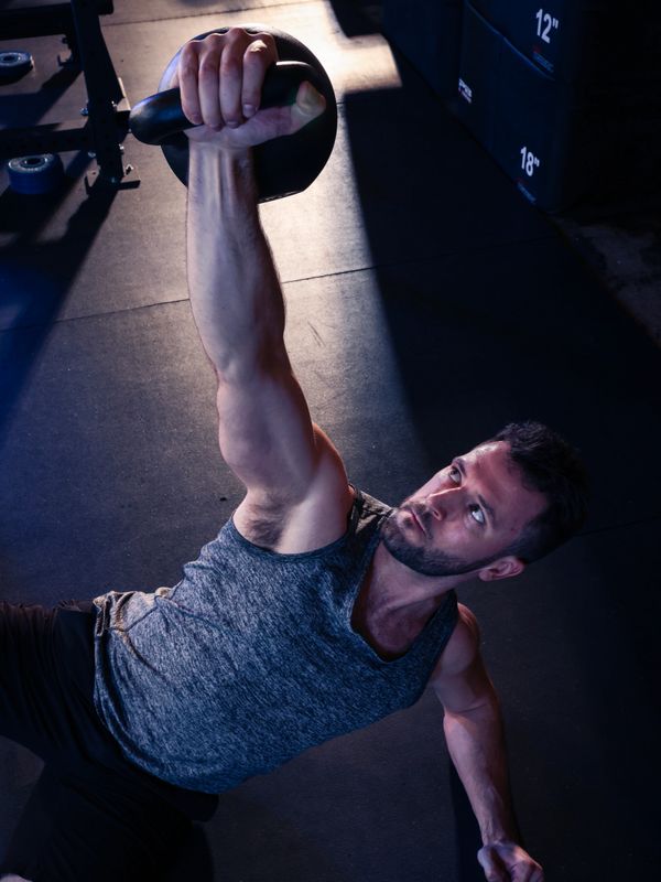 Man lifting a kettlebell while lying down in a gym.