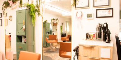 Bright, modern hair salon with tan chairs and green plants.