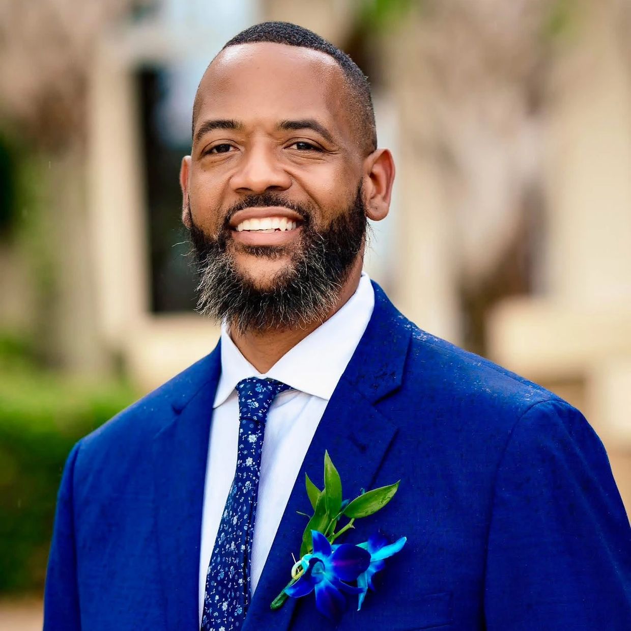 Smiling man in a blue suit with a floral tie and boutonniere.
