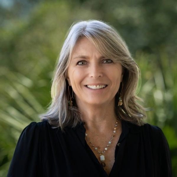 Smiling woman with gray hair wearing a black top outdoors.