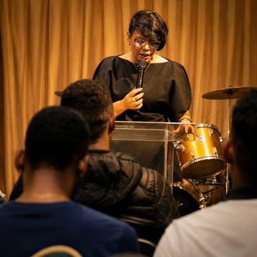 Woman speaking into a microphone at a podium in front of an audience.