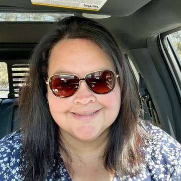 Smiling woman wearing sunglasses inside a car.