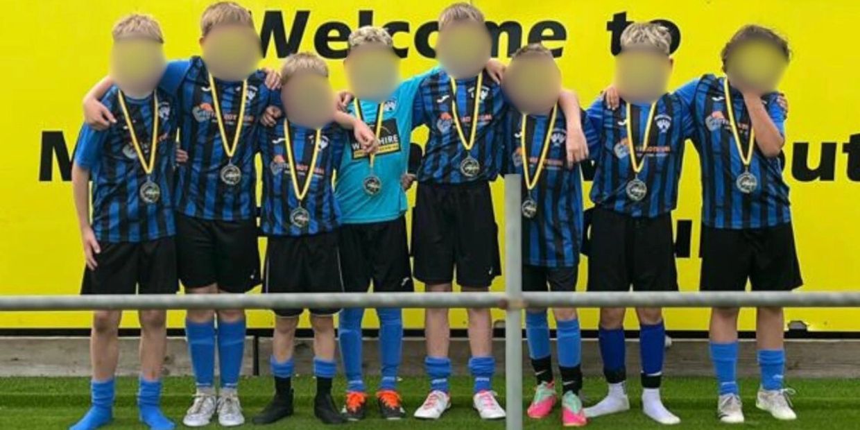 Young soccer team wearing medals posing for a group photo in front of a yellow sign.