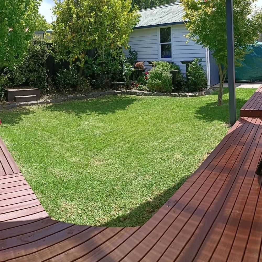 Backyard with green lawn, wooden deck, and garden shed surrounded by trees and bushes.