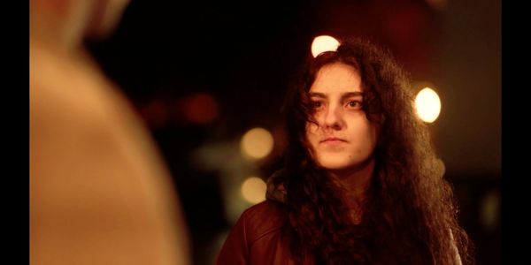 A woman with curly hair looks thoughtfully in a dimly lit setting.